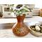 A handmade gourd vase sits on a coffee table. The vase is a warm brown with a cat drawn in a light tan. 